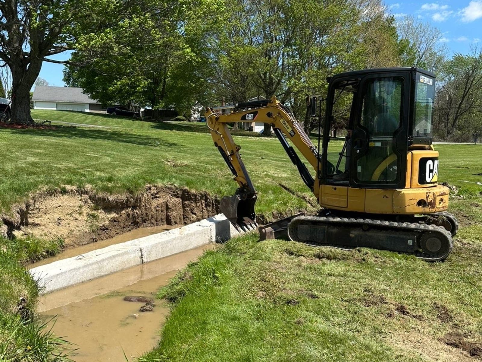 Mini excavator and concrete outlet headwall on a Pittsburgh drainage ditch